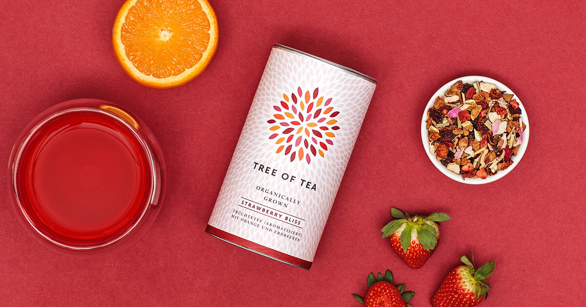 Tree of Tea Strawberry Bliss Früchtetee und daneben ein Glas Tee und Erdbeeren