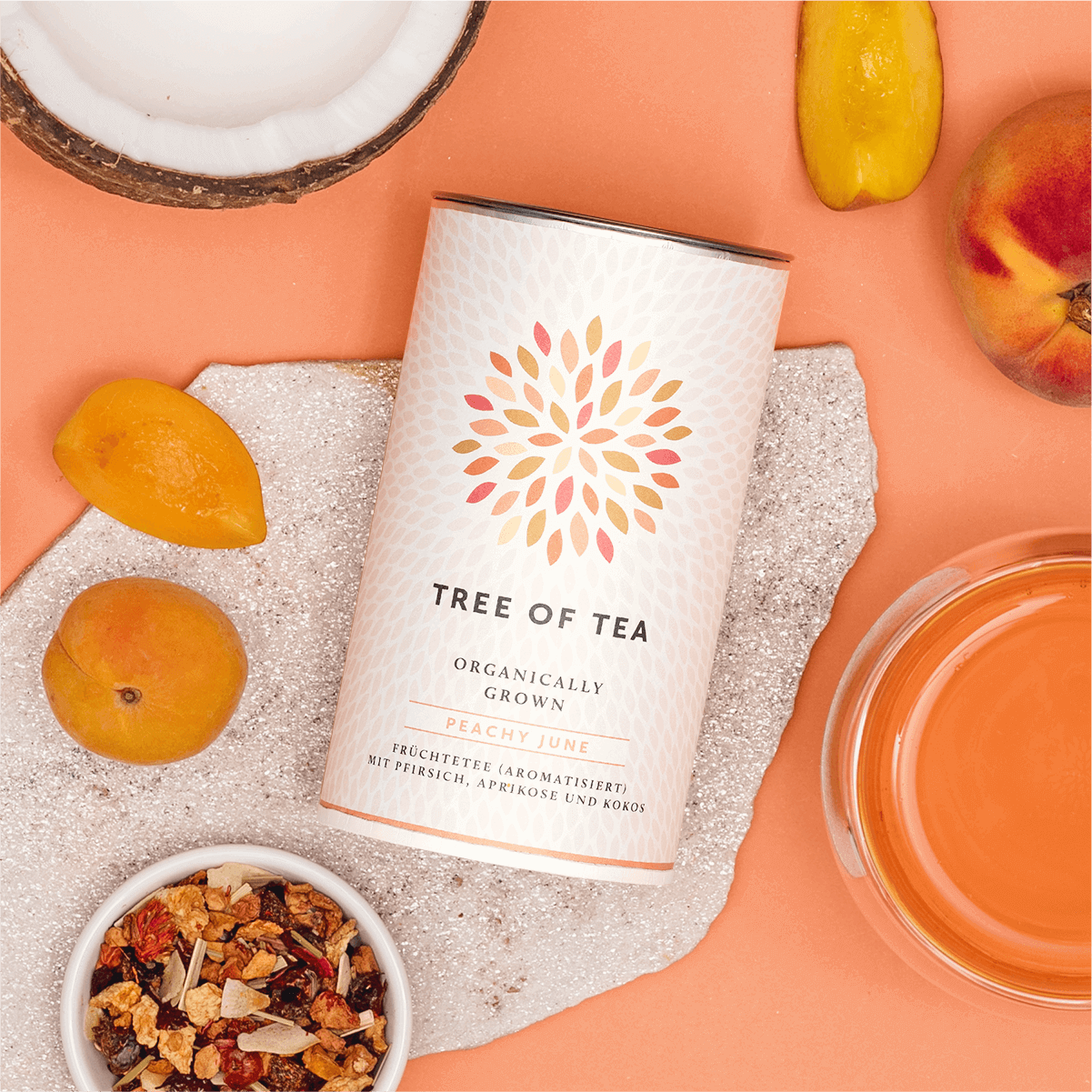 Tree of Tea Peachy June liegend neben einem Glas Tee, Pfirsichen und einer halben Kokosnuss