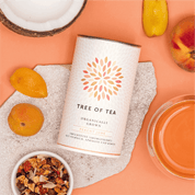 Tree of Tea Peachy June liegend neben einem Glas Tee, Pfirsichen und einer halben Kokosnuss
