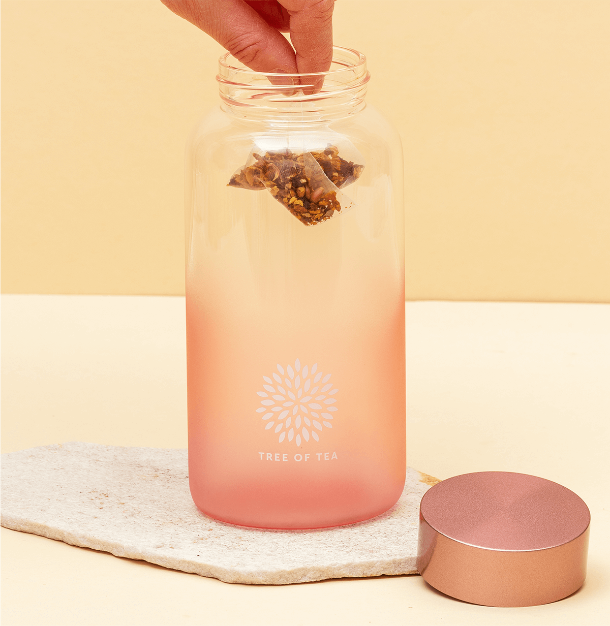 Aufgeschraubten Ice Tea Flasche in Rosa, in der eine Hand einen Tree of Tea Teebeutel hineinführt.