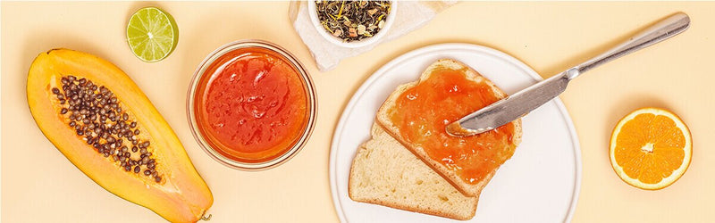 Papaya Orangen Marmelade auf einem Brot mit einer halben Papaya daneben