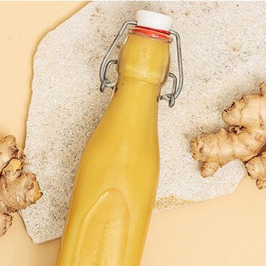 Ginger Glow Shots in einer Flasche mit Ingwer, Apfel, Tee und Zitrone daneben