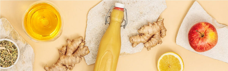 Ginger Glow Shots in einer Flasche mit Ingwer, Apfel, Tee und Zitrone daneben