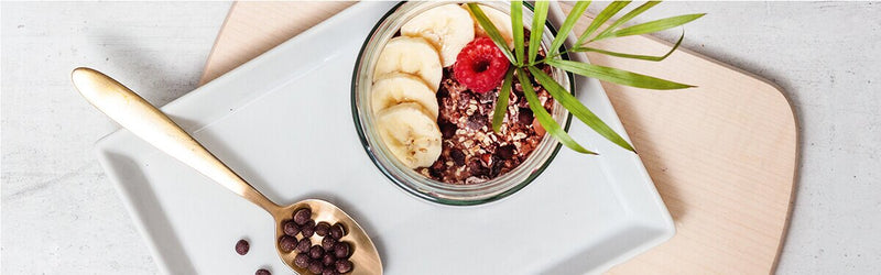 Banane Schoko Overnight Oats in einem Glas mit Bananenscheiben und einem Löffel daneben