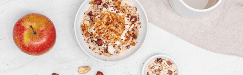 Bircher Müsli in der Schüssel mit Nüssen dekoriert und einem Apfel daneben