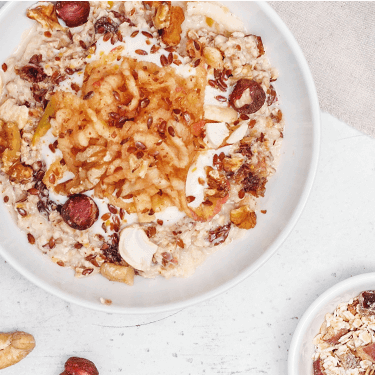 Bircher Müsli in der Schüssel mit Nüssen dekoriert und einem Apfel daneben