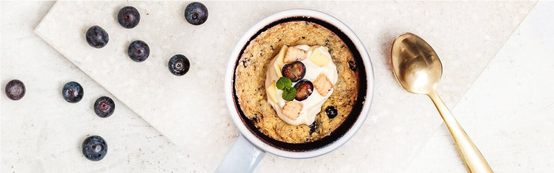 Blueberry Tassenkuchen in einer Schale mit Heidelbeeren und goldenem Löffel daneben