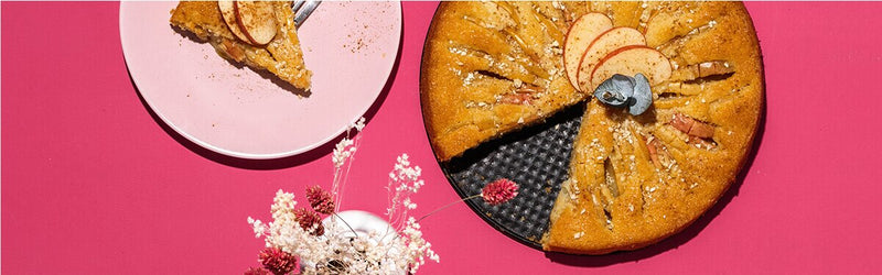 Apfelkuchen in einer Springform und daneben ein Teller mit einem Kuchenstück