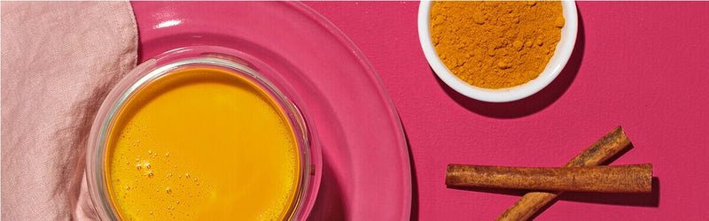 Kurkuma Latte mit Kurkuma und Zimtstangen daneben