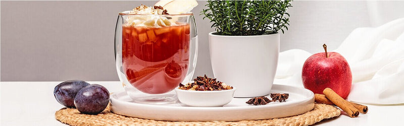 Bratapfel Punsch mit Zimtsahne, mit einem Apfel, Pflaumen, Tee und Gewürzen daneben