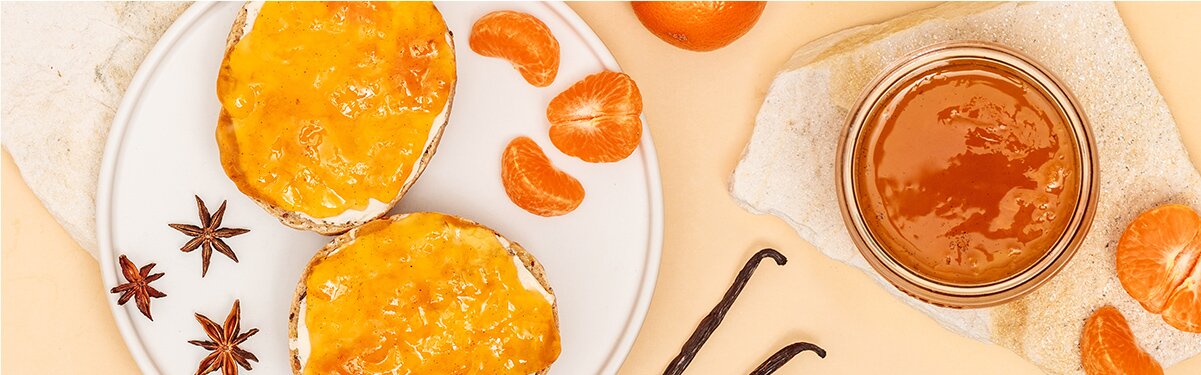 Zwei Scheiben Brot mit Mandarinen Marmelade auf einem Teller undMandarinen Marmelade mit Mandarinen daneben