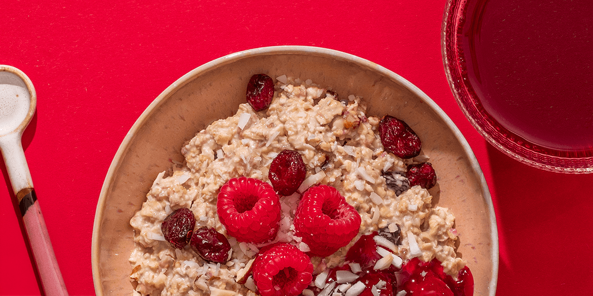 Eine Draufsicht auf ein Frühstücks-Arrangement auf braunem Grund: Eine schwarze mymuesli-Dose, eine Schüssel mit Müsli und eine Tasse Kaffee mit Milchschaum.