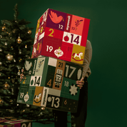 Person trägt 2 mymuesli Adventskalender vor einen Weihanchtsbaum