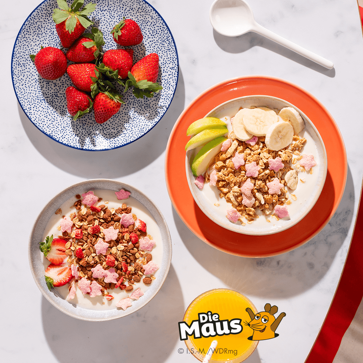 Mymuesli bio Superelefanten-Müsli und
Mymuesli bio Supermaus-Müsli im Probierpaket in Schalen mit frischen Erdbeeren und frischen Äpfeln von oben.