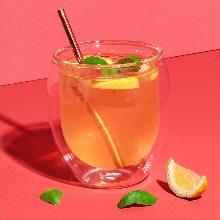 White Tropical Cocktail mit Zitronenstücken, Basilikum und Strohhalm