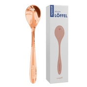 Ein glänzender, kupferfarbener mymuesli -Löffel (Rosegold) steht aufrecht neben seiner weißen Verkaufsverpackung auf schwarzem Hintergrund.