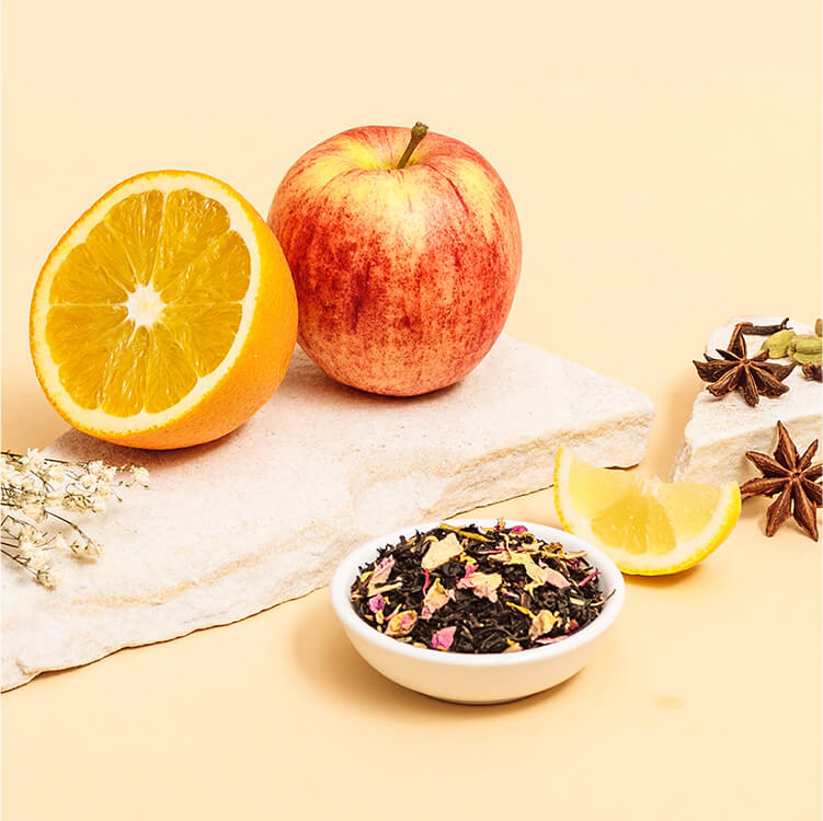 Schwarztee in einer Schüssel und daneben ein Apfel und Orange